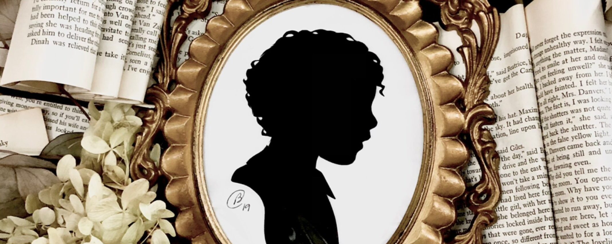silhouette of a little boy framed in a gold frame laid atop book pages and dried hydrangea blooms